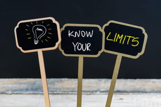 Concept message KNOW YOUR LIMITS and light bulb as symbol for idea written with chalk on wooden mini blackboard labels, defocused chalkboard and wood table in background