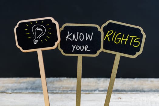 Concept message KNOW YOUR RIGHTS and light bulb as symbol for idea written with chalk on wooden mini blackboard labels, defocused chalkboard and wood table in background