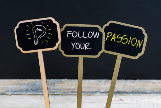 Concept message FOLLOW YOUR PASSION and light bulb as symbol for idea written with chalk on wooden mini blackboard labels, defocused chalkboard and wood table in background