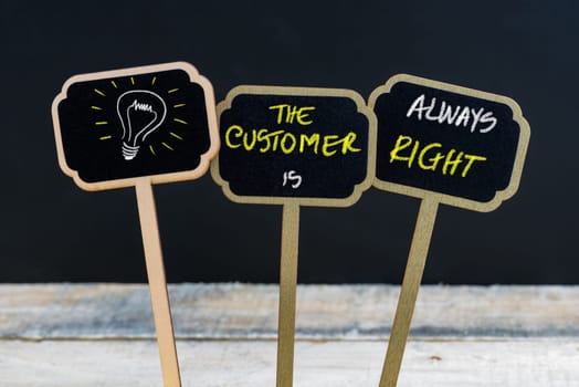 Concept message THE CUSTOMER IS ALWAYS RIGHT and light bulb as symbol for idea written with chalk on wooden mini blackboard labels, defocused chalkboard and wood table in background