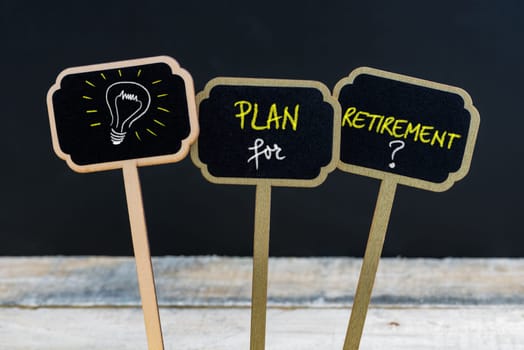 Concept message PLAN FOR RETIREMENT and light bulb as symbol for idea written with chalk on wooden mini blackboard labels, defocused chalkboard and wood table in background