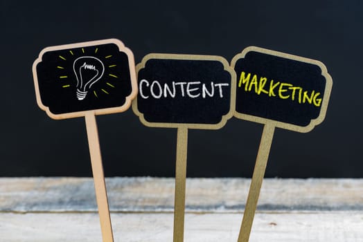Concept message CONTENT MARKETING and light bulb as symbol for idea written with chalk on wooden mini blackboard labels, defocused chalkboard and wood table in background