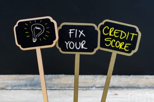Concept message FIX YOUR CREDIT SCORE and light bulb as symbol for idea written with chalk on wooden mini blackboard labels, defocused chalkboard and wood table in background