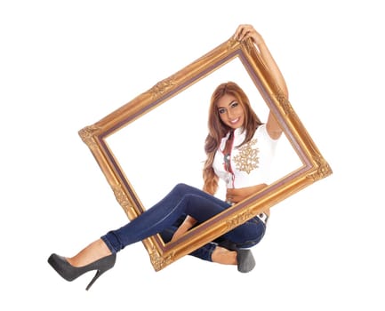 A beautiful young woman sitting in jeans with one leg trough a picture.frame, isolated for white background..