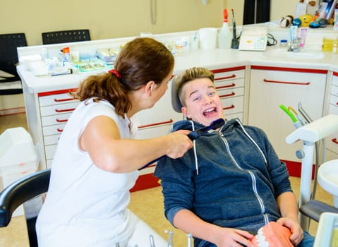 teenager is treated by female dentist in dental surgery
