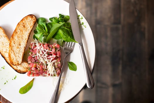 Tartare of beef with spinach on a white plate. Isolated on black.