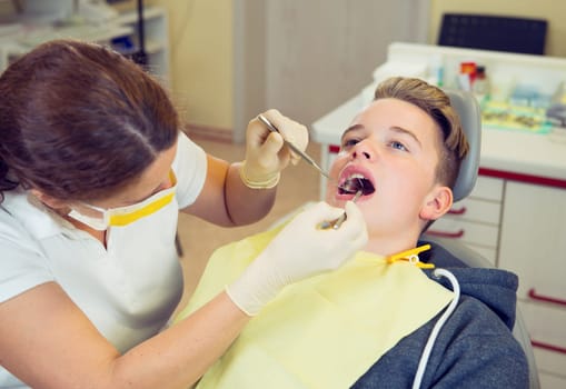 teenager is treated by female dentist in dental surgery
