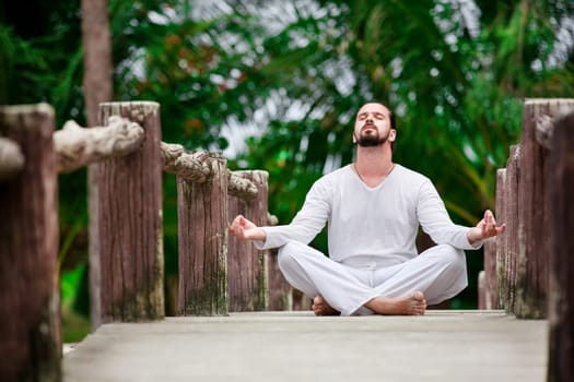 man wearingwhite doing yoga in tropic jungle bridge