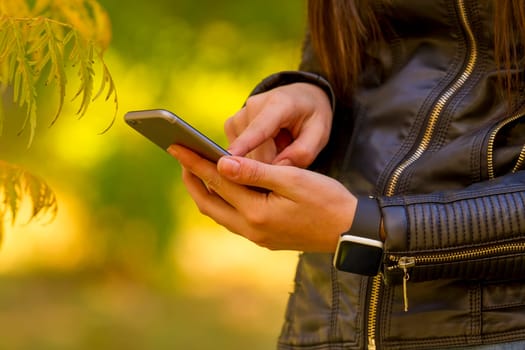 Young girl using smart phone in the park, wears smart watch in everyday lifestyle. Focus on smart phone!
