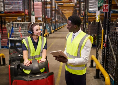 Warehouse manager and woman on tow tractor in discussion