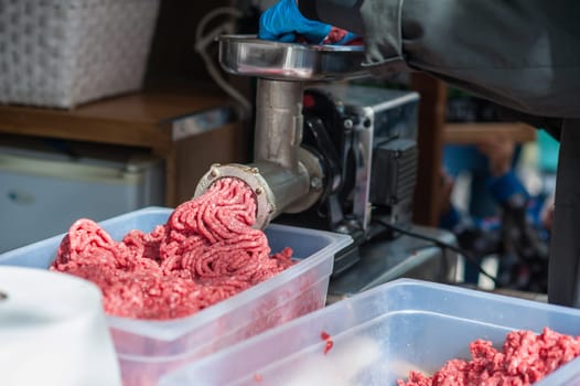 Tray of fresh minced meat. Butcher hand meat grinder and machine that puts the meat back into the machine.