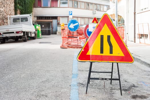 Road sign lane narrowing. In the background, blurred a roadworks