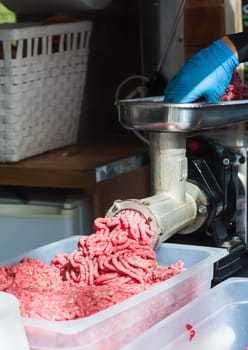 Tray of fresh minced meat. Butcher hand meat grinder and machine that puts the meat back into the machine.