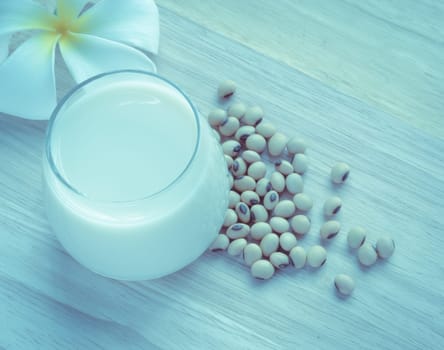 Fresh Soy milk (Soya milk) and dried soybean seeds on wooden background with white plumeria flower. Retro-Vintage filter effect