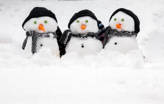 Three cute snowmen in a row sat in the snow wearing hats and scarfs. Copy space for text below