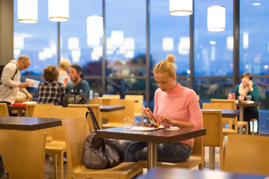 Young female traveler eating pizza at airport restaurant while waiting for late night flight departure.