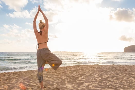 Active young woman practicing yoga on beach at sunset.