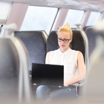 Businesswoman sitting and traveling by train working on laptop. Business travel concept.