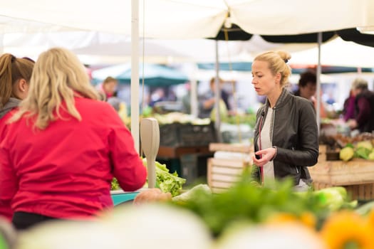 Woman buying fruits and vegetables at local food market. Market stall with variety of organic vegetable.