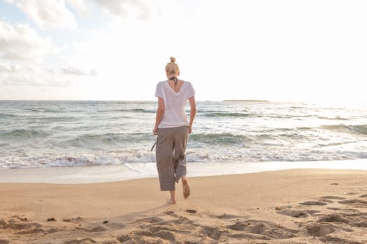 Woman walking on sand beach at golden hour. Seashore sunset walk.