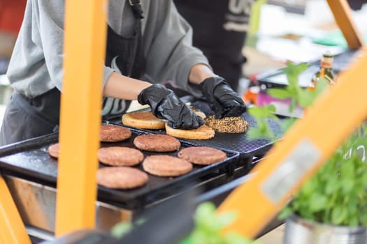 Chef making beef burgers outdoor on open kitchen international food festival event. Street food ready to serve on a food stall.