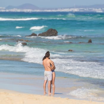 Young couple embracing, enjoying vacations on El Corralejo beach, famous holiday destination on Fuerteventura, Canary Islands, Spain.