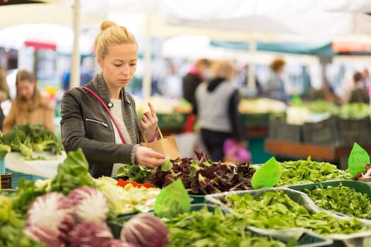 Woman buying fruits and vegetables at local food market. Market stall with variety of organic vegetable.
