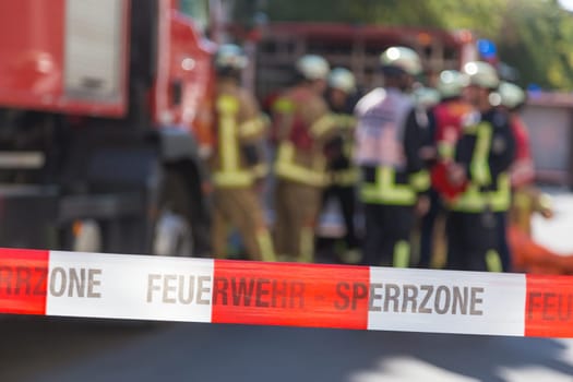 Team of blured firefighters by firetruck on protected accident site. Focus on red and white security band.