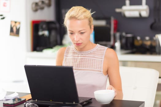 Business woman working remotly from her dining table. Home kitchen in the background.