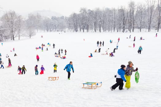 Ljubljana, Slovenia - Jan 3, 2016: Children sledding and having fun on first winter snow in Tivoli city park in Ljubljana on last day of Christmas holidays on January 3, 2016.