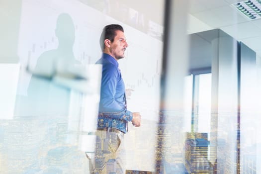 Business man making a presentation in front of whiteboard. Business executive delivering a presentation to his colleagues during meeting or in-house business training. View through glass.