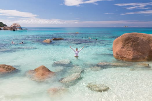 Woman arms rised wearing bikini and lycra top enjoying swimming and snorkeling at amazing Anse Lazio beach on Praslin Island, Seychelles. Summer vacations on picture perfect tropical beach concept.