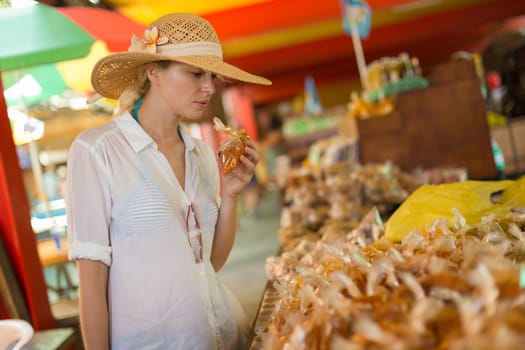 Female traveler wearing elegant colonial style white tunic and hat buying spices on traditional Victoria food market on Seychelles islands.