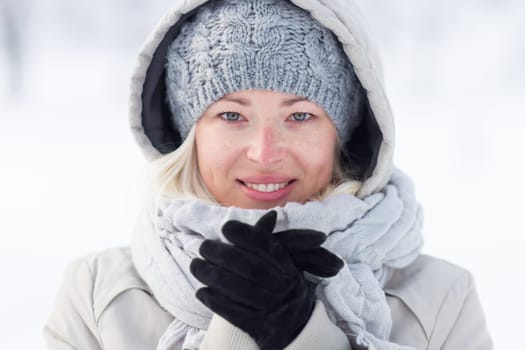 Girl wearing gloves, beeing cold outdoors in winter. Beautiful winter portrait of young woman in the winter snowy scenery.