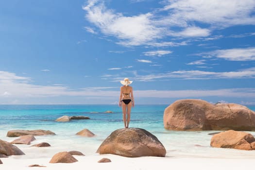 Woman wearing black bikini and beach hat, enjoying amazing view on Anse Lazio beach on Praslin Island, Seychelles. Summer vacations on picture perfect tropical beach concept.