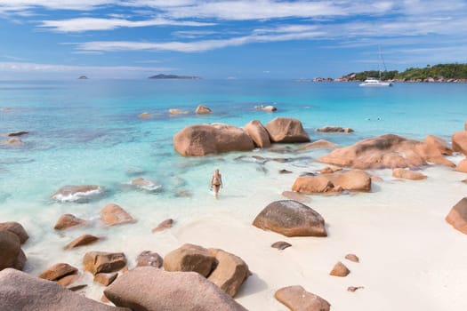 Happy woman arms rised wearing stylish bikini enjoying swimming and snorkeling at amazing Anse Lazio beach on Praslin Island, Seychelles. Summer vacations on picture perfect tropical beach concept.