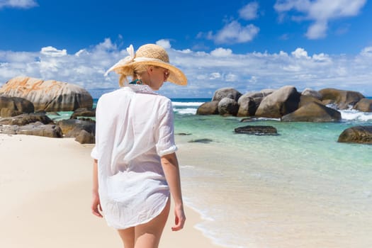 Woman wearing white loose tunic over bikini and beach hat on Mahe Island, Seychelles. Summer vacations on picture perfect tropical beach concept.
