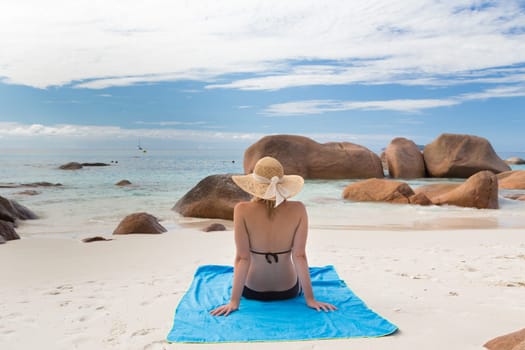 Woman wearing black bikini and beach hat, sunbathing at Anse Lazio beach on Praslin Island, Seychelles. Summer vacations on picture perfect tropical beach concept.