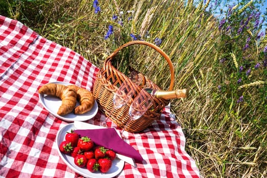 picnic blanket with champagne, strawberries and croissant