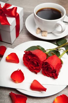 red roses, cup of coffee and present on a table