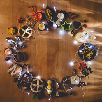 Christmas treats, accessories and fairy lights presented in a circle on a wooden chopping board.