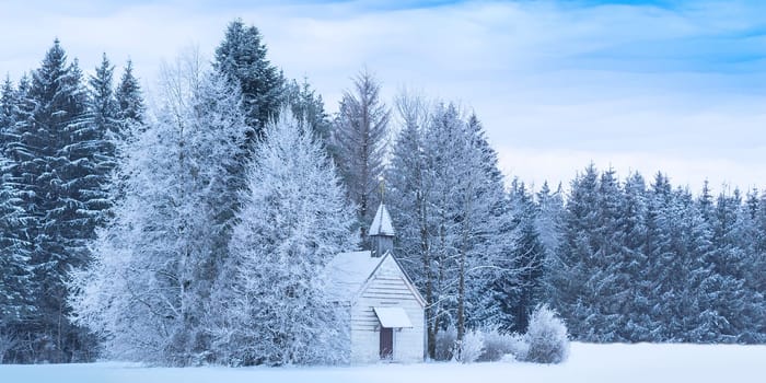 Christmas serene winter panoramic landscape with tiny woody chapel in snowy frozen forest