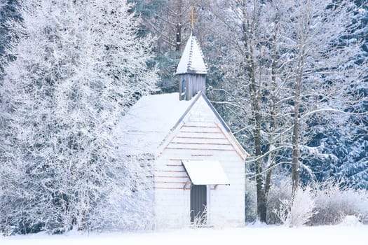 Small woody chapel in frozen snowy forest. Stock photo captured in Bavarian Alpine rural region Allgaeu.