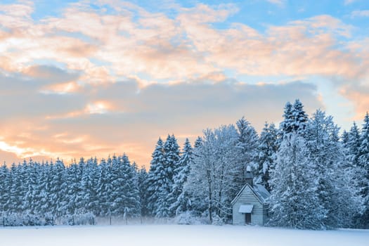 Small wooden chapel in snowbound frosty forest under morning sunrise sky. Amazing idyllic winter landscape in Bavarian rural region Allgaeu.