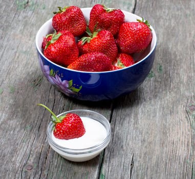 plate strawberry and one strawberry in a saucer with cream, on a wooden table, a subject of berry and desserts