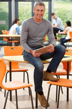 Male Tutor Sitting In Classroom With Digital Tablet