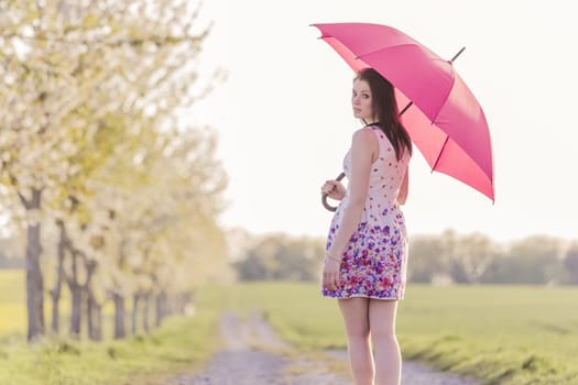 The weather is changeable between sun and rain. The attractive young woman goes for a walk on a path in nature.