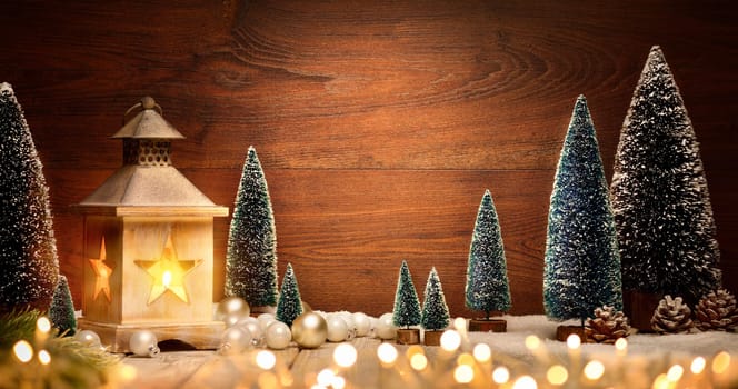 Christmas scene with a lantern,trees,baubles and blurred lights in front of an illuminated elegant dark wooden board as copy space