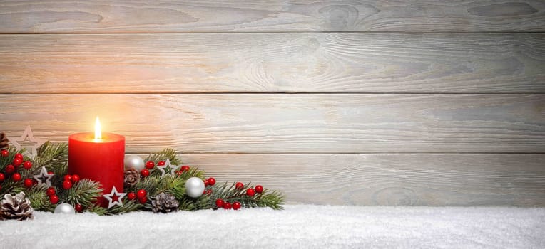 Christmas or Advent wood background with a burning candle on snow,decorated with fir branches and ornaments,panoramic format with copy space