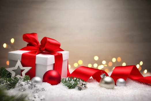 Christmas scene with a white gift box,red bow and ribbon,lights,baubles,fir branches and snow,with copy space